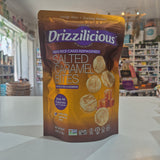 A bag of Drizzilicious Salted Caramel Bites mini rice cakes standing on a white countertop in a blurred retail store setting.