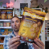A man in a plaid shirt holds up a bag of Drizzilicious French Toast Bites in front of a store shelf filled with other snack products.