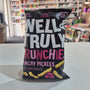 A bag of Well & Truly Crunchies Crunchy Pickles snack chips sits on a white counter in a retail store setting with shelves of products in the background.