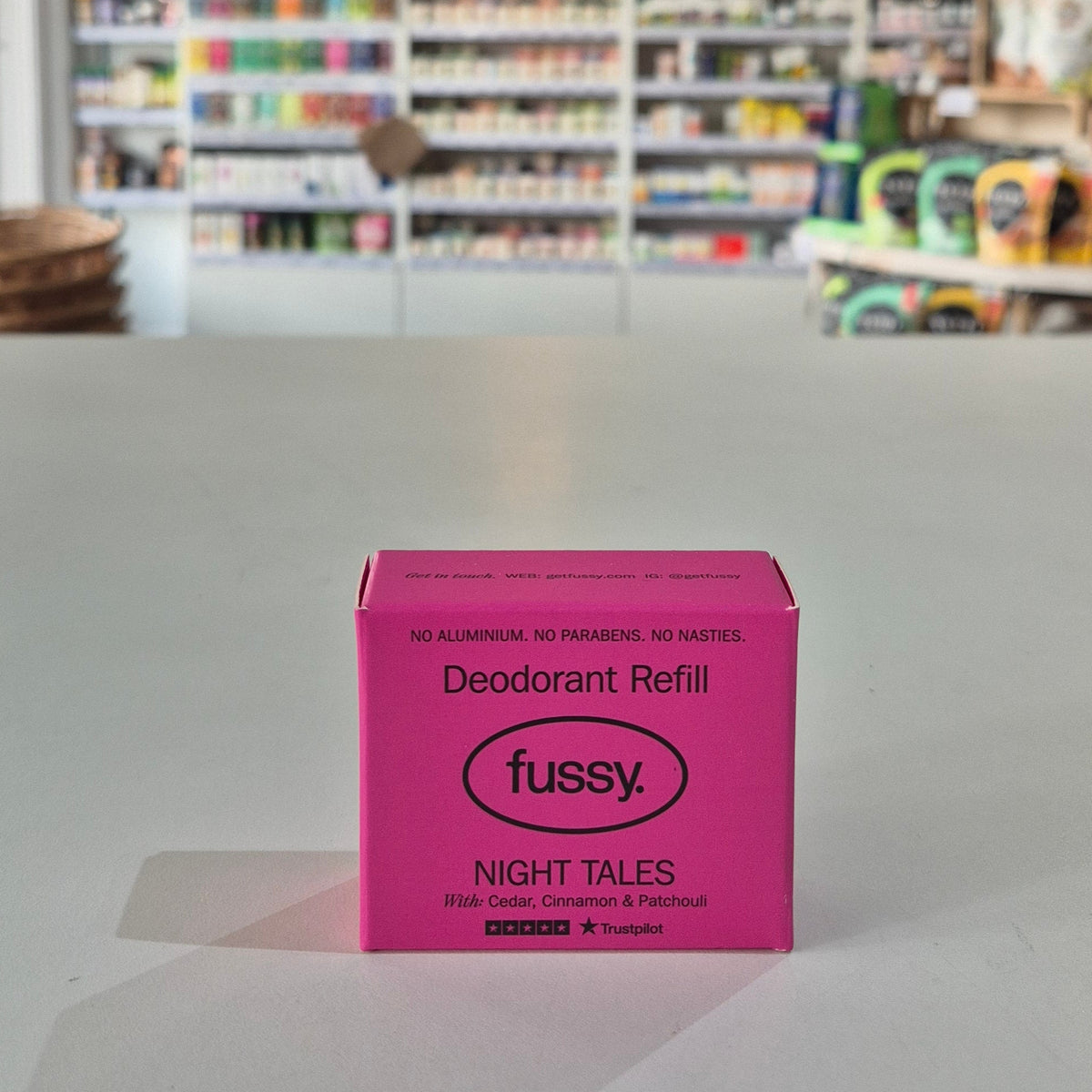 Pink deodorant refill box labeled 'fussy' on a gray surface with a blurred store background.