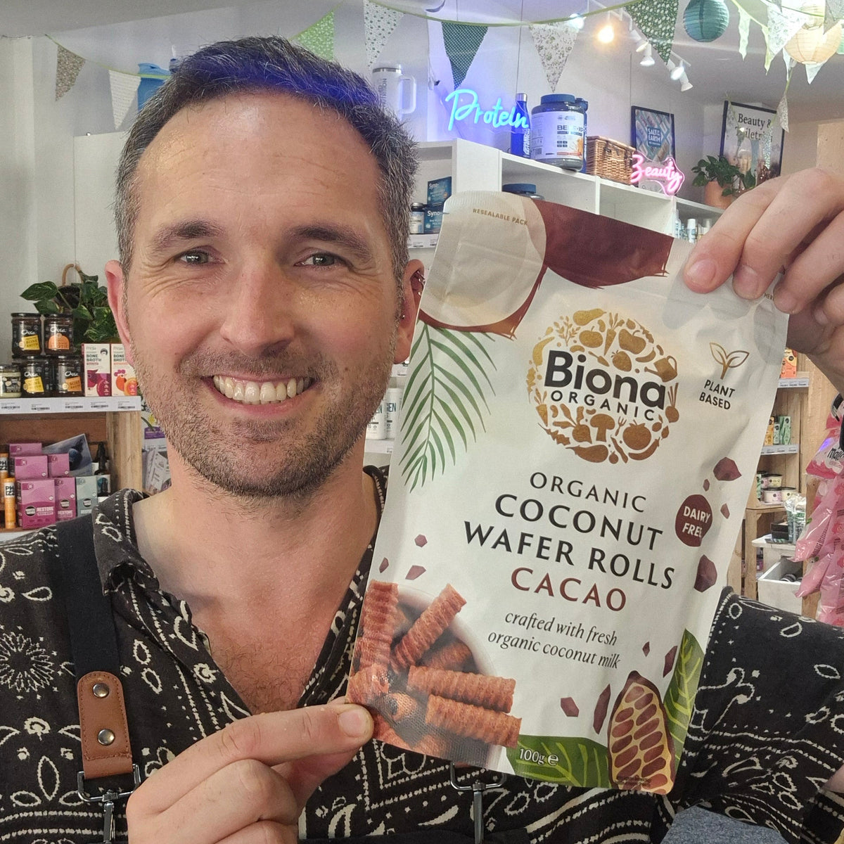 Man holding a package of Biona Organic Coconut Wafer Rolls Cacao in a store setting.