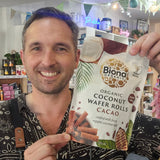 Man holding a package of Biona Organic Coconut Wafer Rolls Cacao in a store setting.