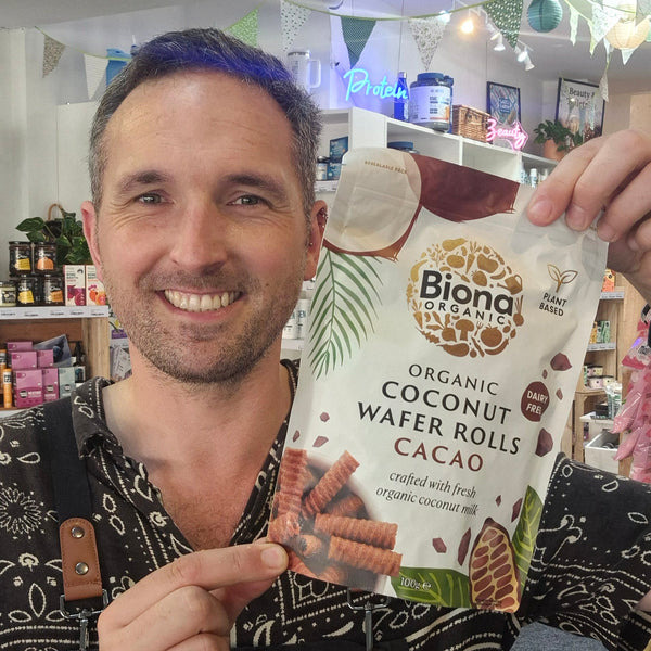 Man holding a package of Biona Organic Coconut Wafer Rolls Cacao in a store setting.