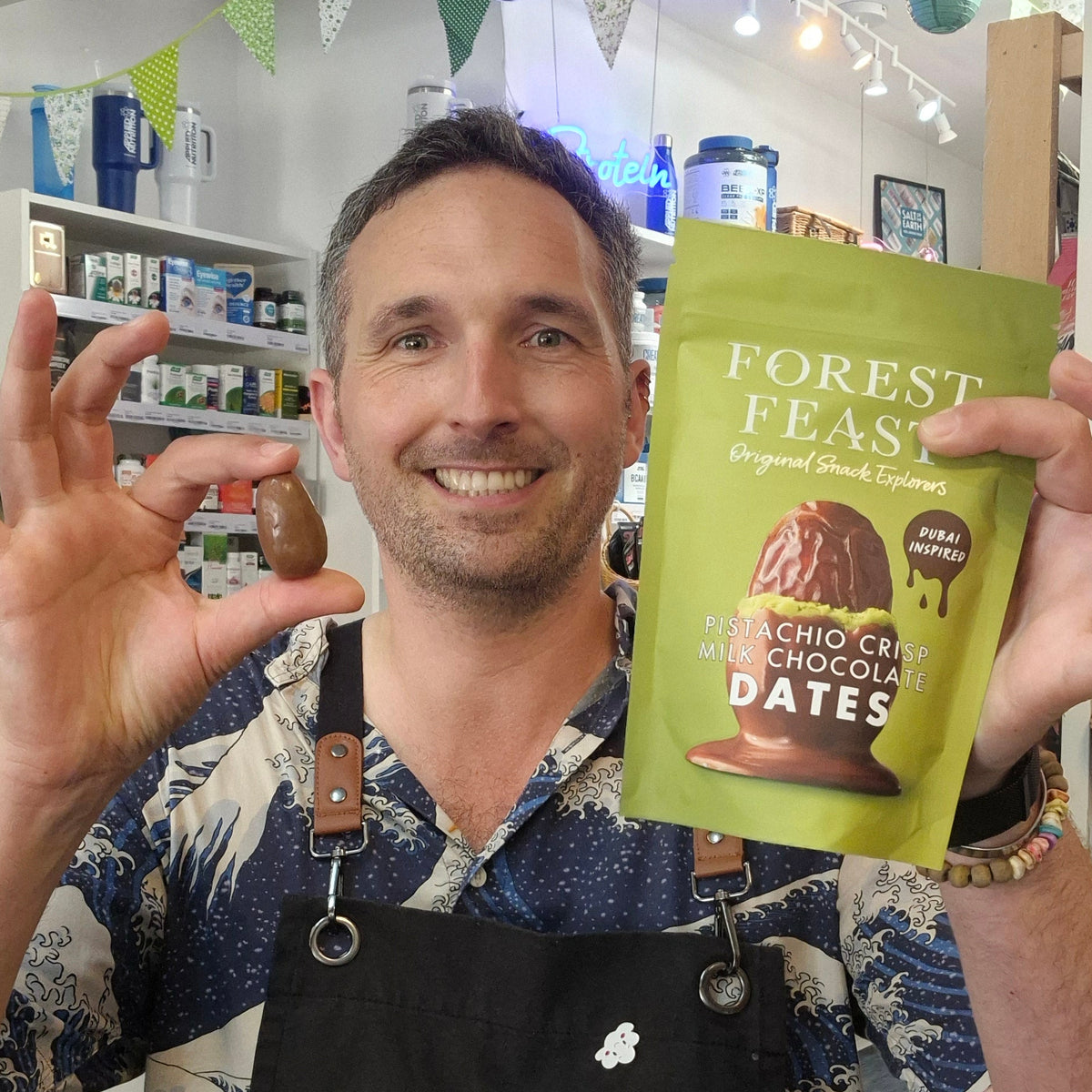 Man holding a package of 'Forest Feast' dates and a single date in a store setting