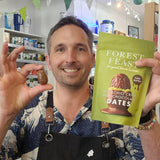 Man holding a package of 'Forest Feast' dates and a single date in a store setting