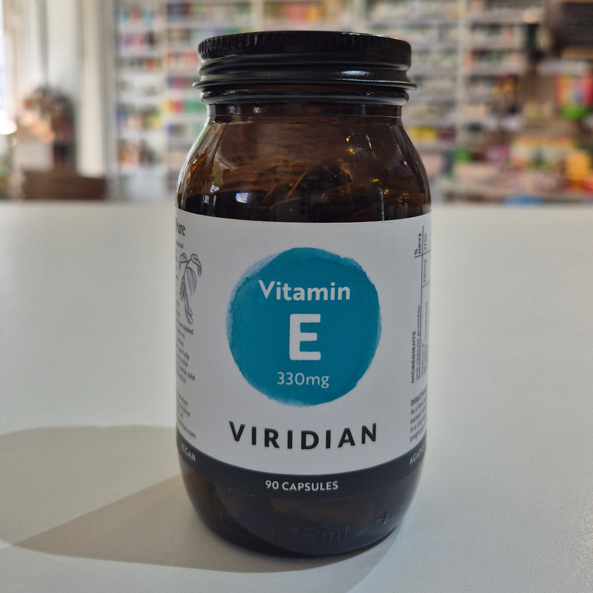 Jar of Viridian Vitamin E capsules on a white surface with a blurred store background