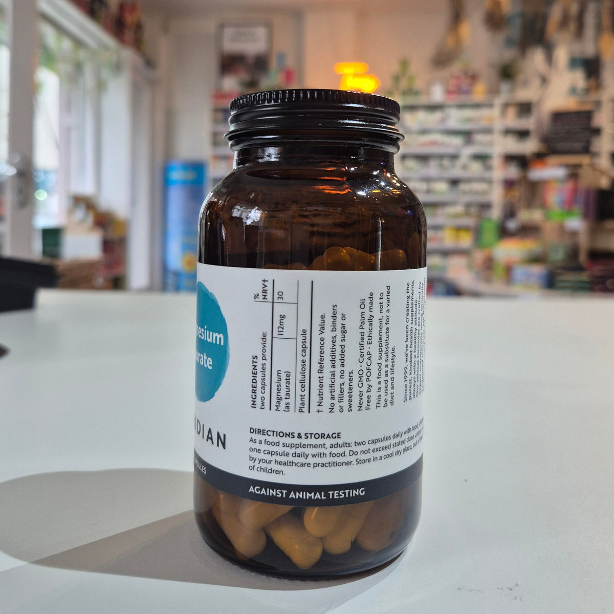 Bottle of Viridian Magnesium Taurate on a counter in a store setting. Brown supplement bottle with label on a white surface, blurred store background