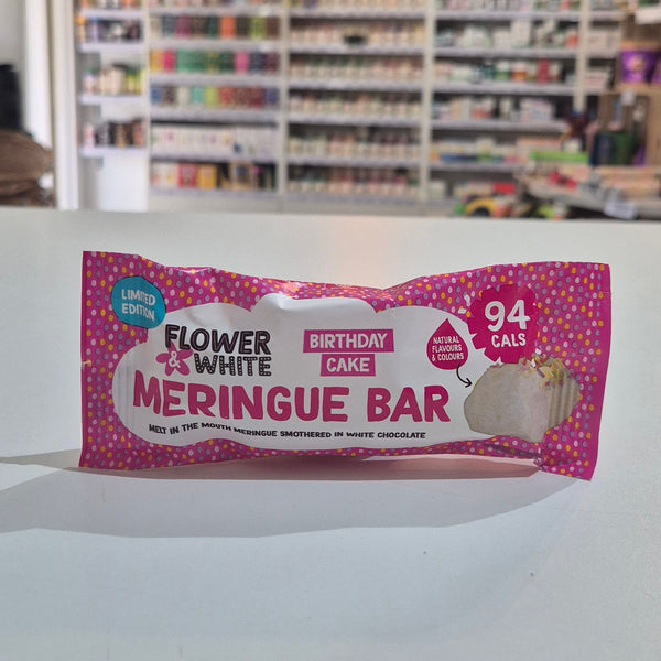 A pink and white packaged snack bar labeled 'Fruity Snacks Meringue Bar' hanging against a white wall, with a blurred store interior visible in the background.