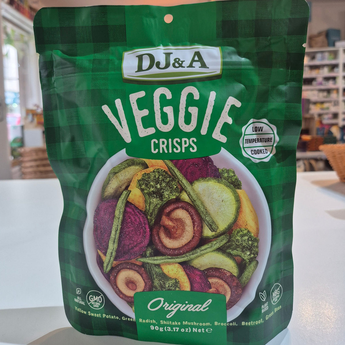 Green package of DJ&A Veggie Crisps with a bowl of colourful vegetables on a white background.