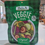 Green package of DJ&A Veggie Crisps with a bowl of colourful vegetables on a white background.