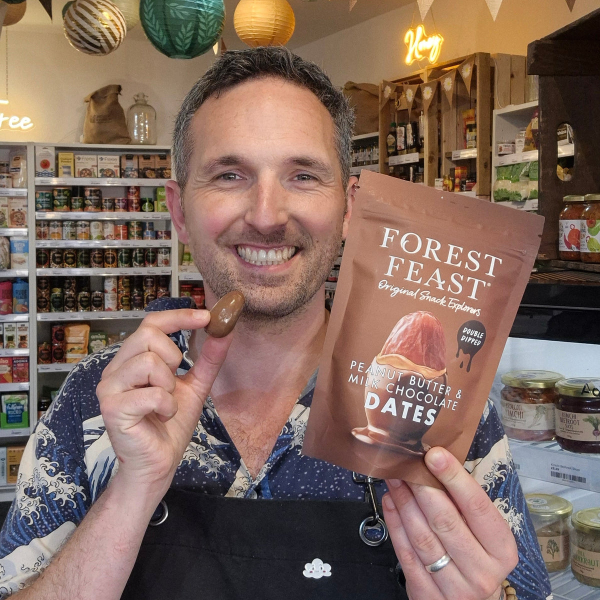 Man holding a package of Forest Feast peanut butter and milk chocolate dates in a store.