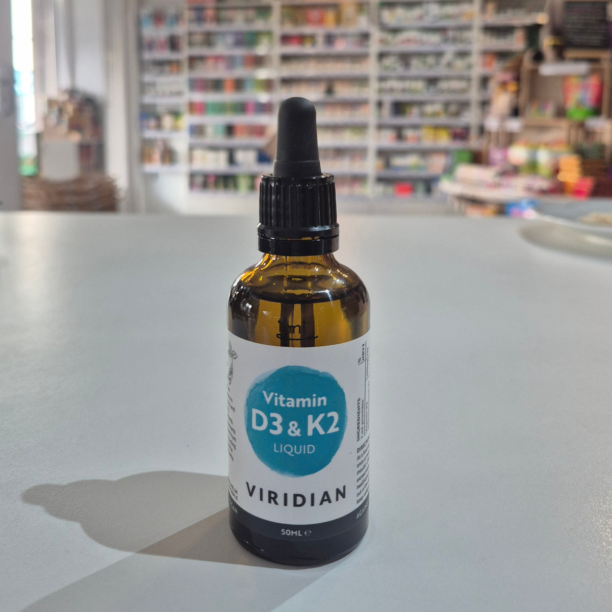 Bottle of Viridian Vitamin D3 & K2 Liquid on a table with a blurred store background