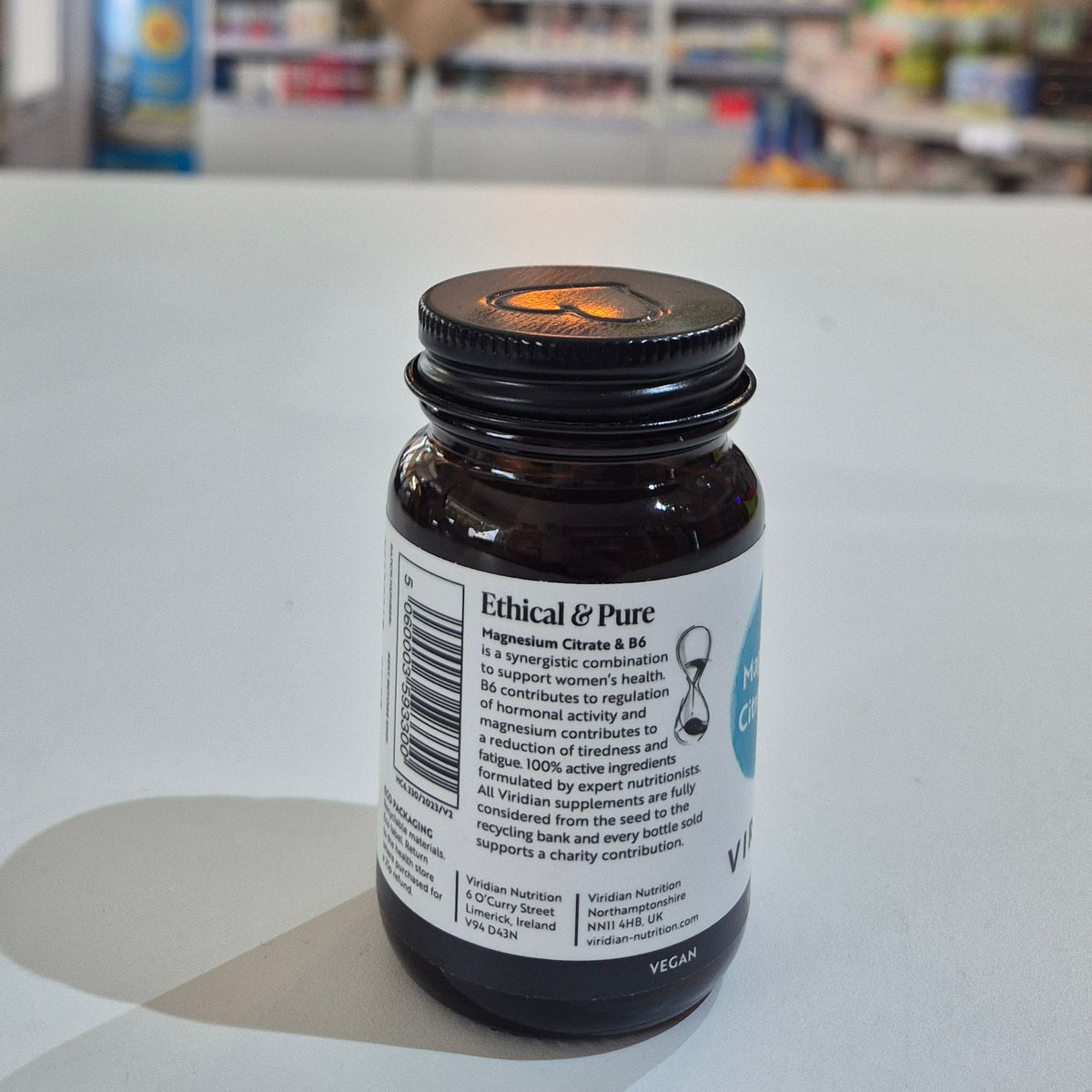 Bottle cap with label on a white surface, blurred background of shelves with products