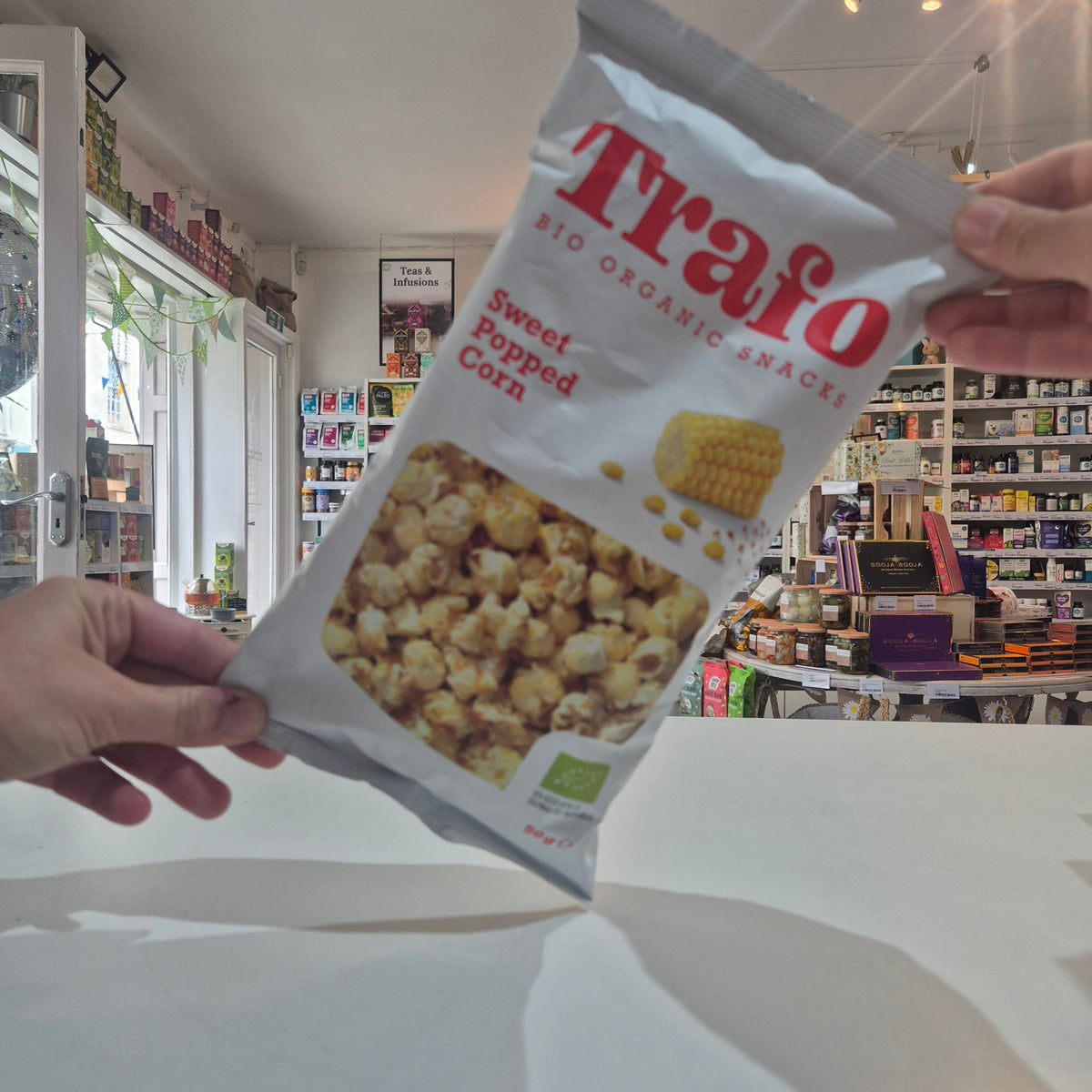 A hand holds a bag of Trafo Sweet Popped Corn organic snack in a retail store setting.