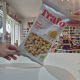 A hand holds a bag of Trafo Sweet Popped Corn organic snack in a retail store setting.