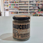 A glass jar of Saucerer Wild Mushroom Truffle Oil pesto with a black lid and brown label, sitting on a white table in a blurred shop interior.