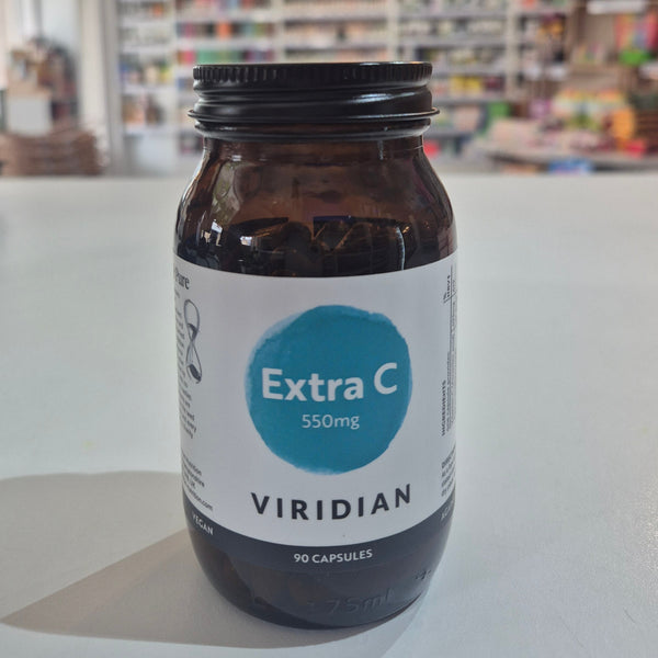 Brown supplement bottle labeled 'Extra C 550mg' by Viridian on a white surface with a blurred store background.