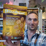 A man in a plaid shirt holds up a large bag of Drizzilicious French Toast Bites in a retail store setting.