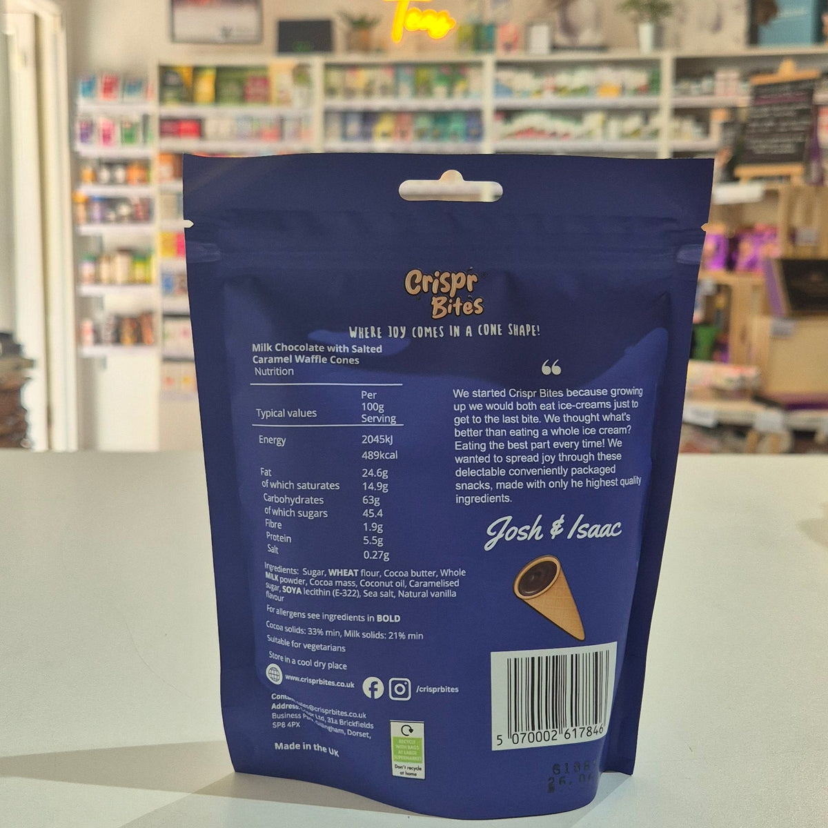 A blue stand-up pouch of back of product Crispr Bites Chocolate Filled Salted Caramel Waffle Cones on a white countertop in a shop setting.