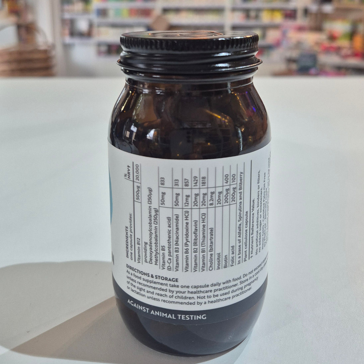 Jar of Viridian High Twelve B12 B Complex supplement on a white surface with a blurred store background.. Brown bottle with label on a white surface, blurred background