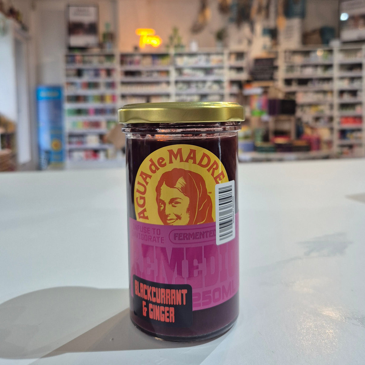 Can of Agua de Madre pepper on a white surface with a blurred store interior in the background.