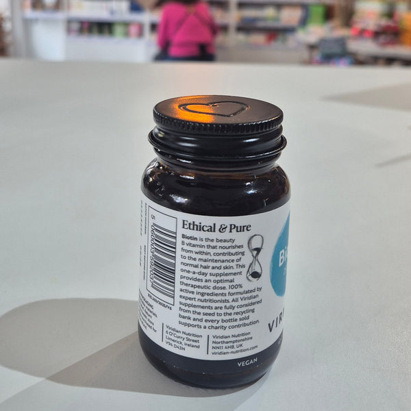 Bottle of Viridian Biotin on a white surface with a blurred store interior in the background. Bottle labeled 'Ethical & Pure' on a light surface with blurred background