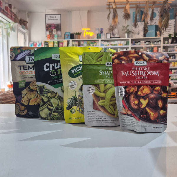 Five bags of DJ&A snack crisps are lined up on a white counter in a retail store setting.