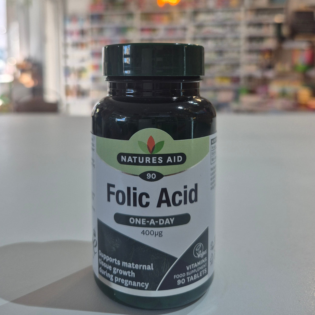 Natures Aid Folic Acid supplement bottle on a white surface with a blurred indoor background