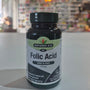 Natures Aid Folic Acid supplement bottle on a white surface with a blurred indoor background