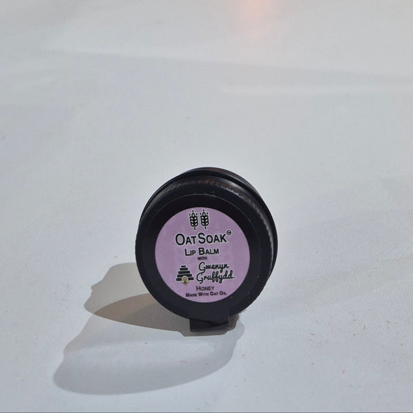 Close-up of a black container with a purple label on a white surface, with a blurred background of shelves and items.