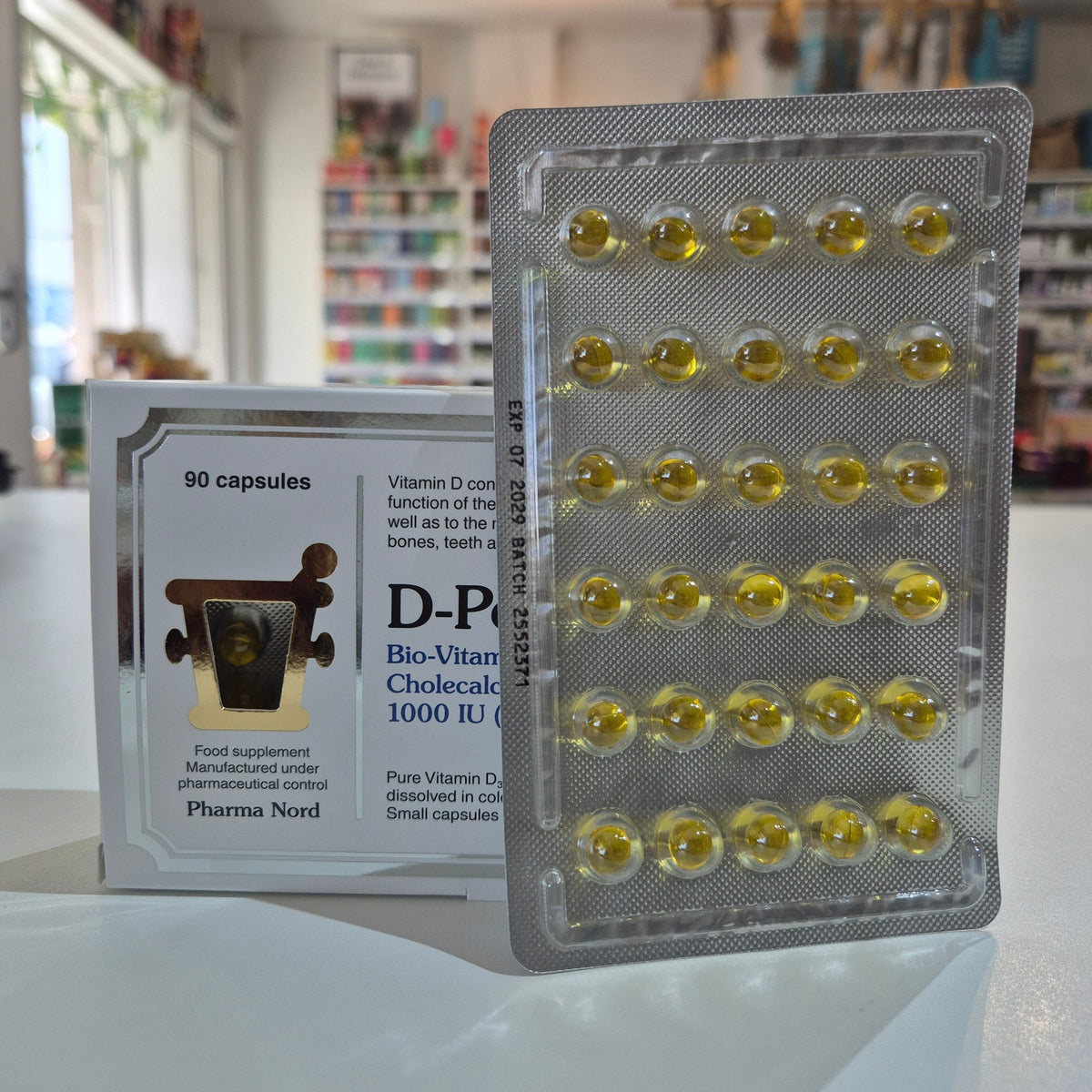 Packaging of Vitamin D capsules with a blurred indoor background