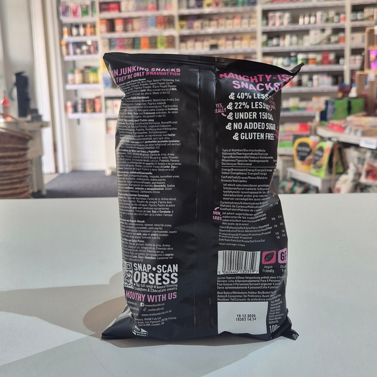 A bag of Well & Truly Crunchies Crunchy Pickles snack chips sits on a white counter in a retail store setting with shelves of products in the background.