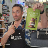 Man in a store holding a 'Forest Feast' snack package, wearing a 'Health & Remedy' apron.