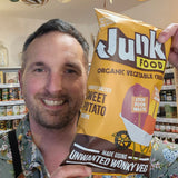 Man holding a bag of 'Junk Food' organic vegetable chips in a store.