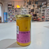 Jar of agua de madre with a label on a white surface, blurred store interior in the background