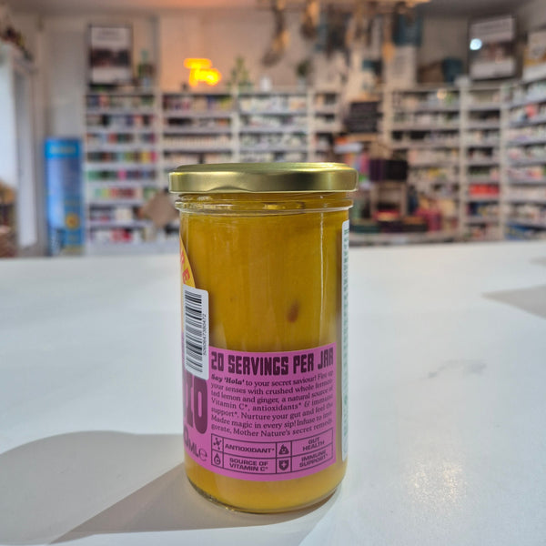 Jar of agua de madre with a label on a white surface, blurred store interior in the background