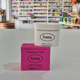 Pink deodorant refill box labeled 'fussy' on a gray surface with a blurred store background.