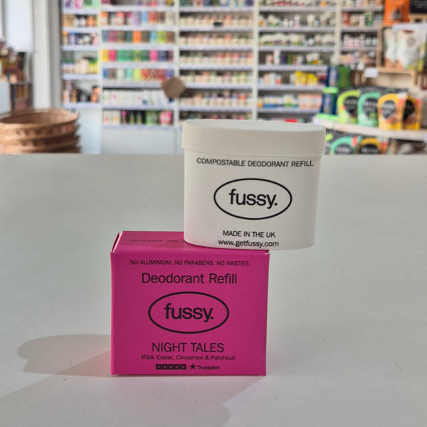 Pink deodorant refill box labeled 'fussy' on a gray surface with a blurred store background.