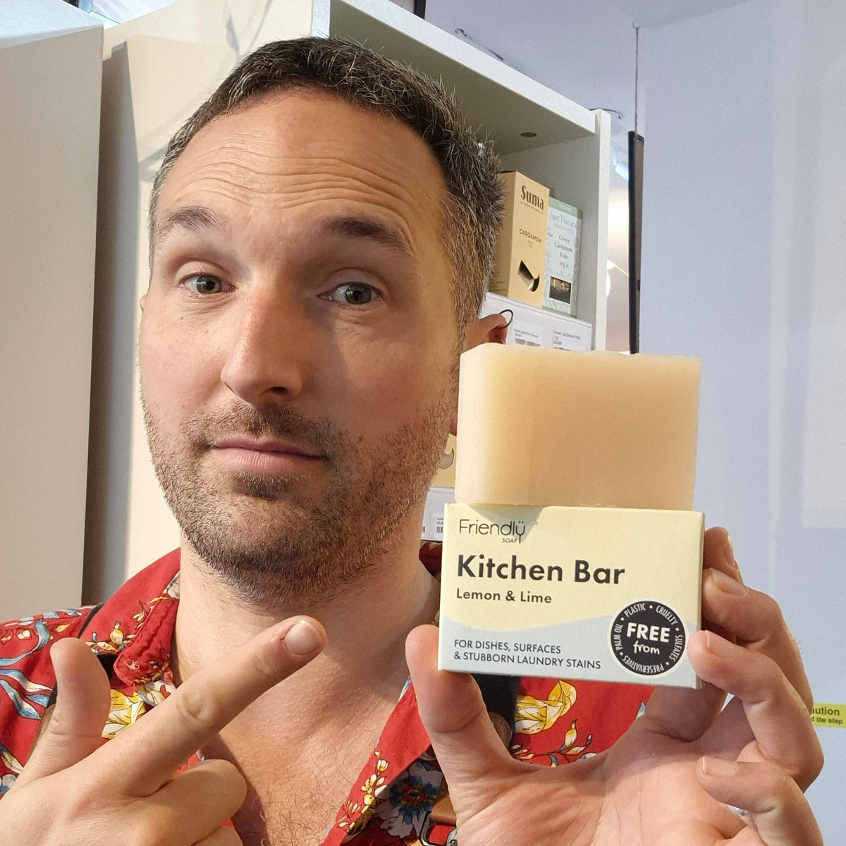 Person holding a bar of Person holding a bar of Kitchen Bar Lemon & Lime Friendly soap with a brand label in a store setting with a label, with another person pointing at it.