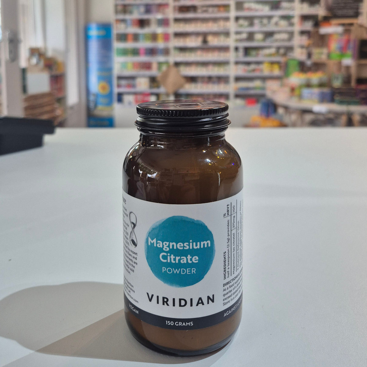 Bottle of Viridian Magnesium Citrate Powder on a white surface with a blurred store background.