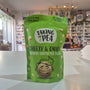 A green bag of Taking the Pea Cheesy & Onion Crunchy Coated Pea Snack standing on a white counter in a store setting with blurred shelves in the background.