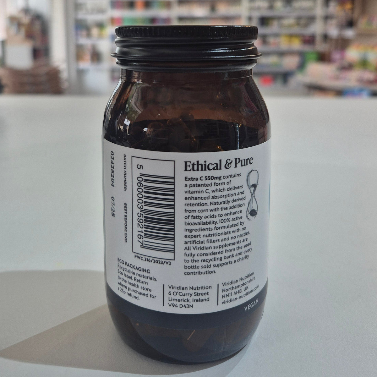 Brown supplement bottle labeled 'Extra C 550mg' by Viridian on a white surface with a blurred store background.