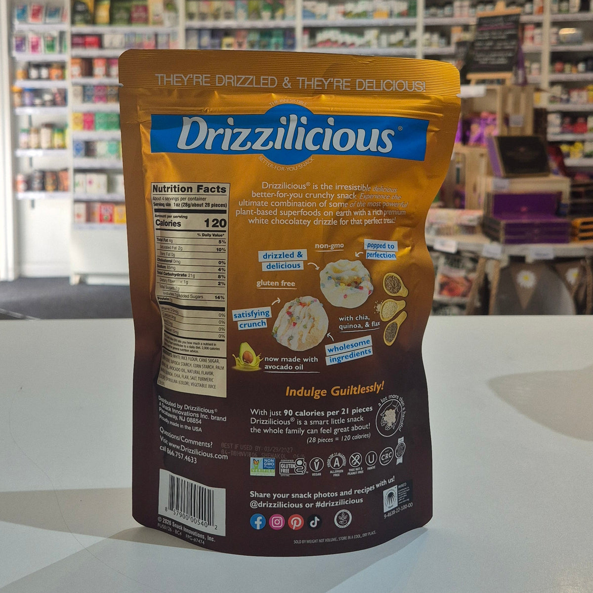 A bag of Drizzlicious snack chips standing upright on a white counter in a retail store, with shelves and fixtures blurred in the background.