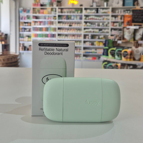 Mint green deodorant container with packaging labeled 'fussy' on a store shelf background.