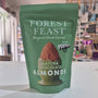 A green stand-up pouch of Forest Feast Matcha Chocolate Almonds, shown standing vertically in a brightly lit indoor space with shelves and decor blurred in the background.