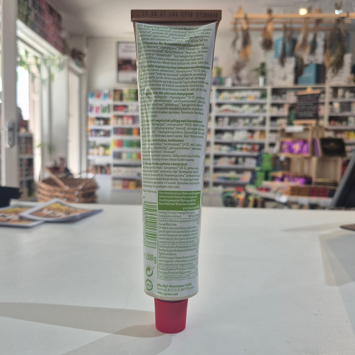 A squeeze tube of Tartex pate, lying horizontally on a white surface with a blurred store background.