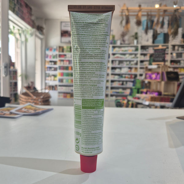 A squeeze tube of Tartex pate, lying horizontally on a white surface with a blurred store background.