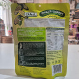 A yellow and green stand-up pouch of D&J&A Pickle-Licious showing the back of the package with ingredients and nutrition facts, set on a white surface in a shop.