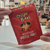A person holds a red bag of Crispr Bites Dark Chocolate Filled Waffle Cones in a brightly lit shop interior.
