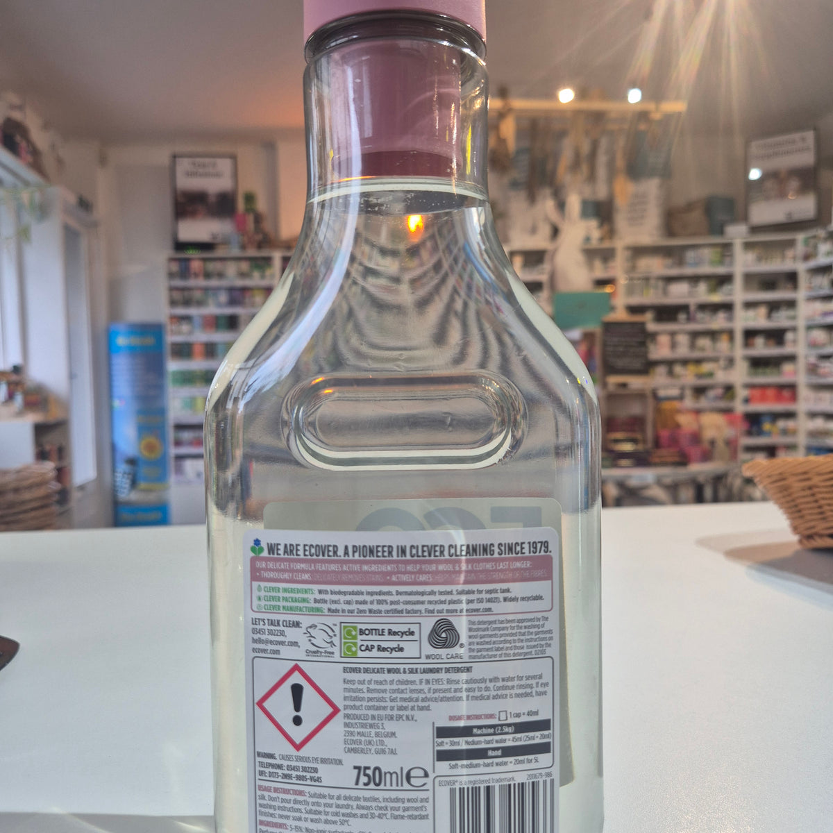Clear glass bottle with a pink cap on a white surface, blurred background